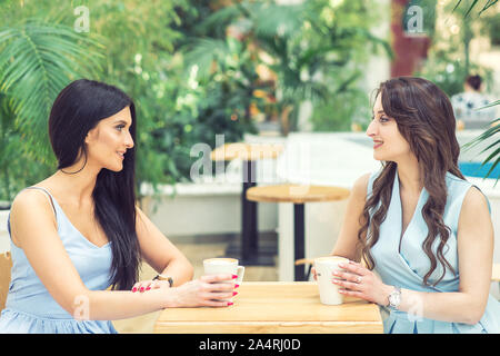 Seitliche Sicht auf zwei schöne Mädchen mit einer Tasse Kaffee im Cafe im Freien. Freunde Chatten in bar an. Stockfoto