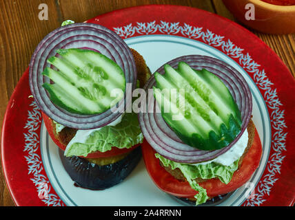 Griechische Lamm Burger, gekrönt mit Tzatziki, Feta, Tomaten, roten Zwiebeln, und geschreddert Kopfsalat Stockfoto