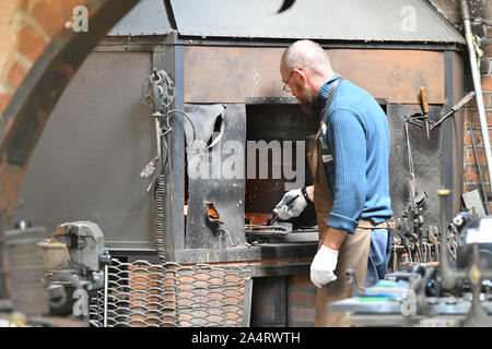 Ein erfahrener Schmied arbeitet mit offenen Feuer. Ein Schmied erlischt die Flamme in einer Schmiede mit einem Funken Feuerwerk, Schmieden heißes Eisen in einem Workshop Stockfoto