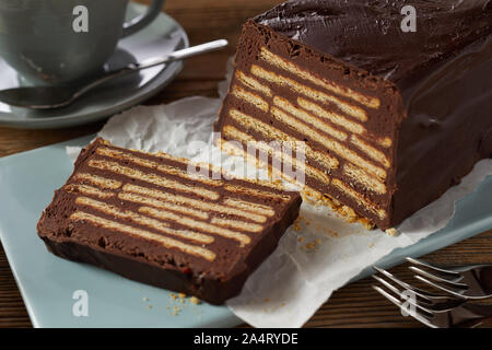 Stück Schokolade-geformten Kuchen mit Keksen Stücke im Inneren, auf Keramik Tablett serviert mit Tasse Kaffee. In enger gesehen - bis auf hölzernen Tisch Stockfoto