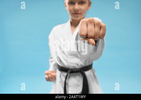 Nahaufnahme des ersten, Position des Karate. Zuversichtlich junior üben Stanzen. Junge Mädchen in weißen Kimono mit schwarzem Gürtel posiert auf blauem Hintergrund in s Stockfoto