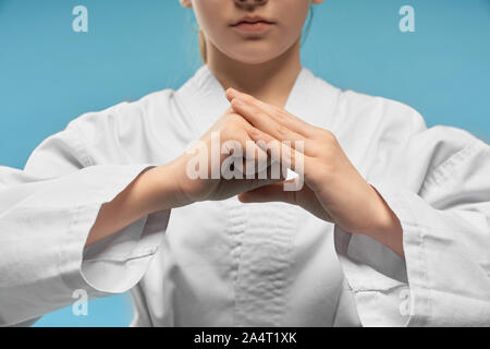 Selektiver Fokus der kleinen Hände des Mädchens zeigt Faust. Hände Position des Karate. Weiblich Kind im weissen Kimono an Kamera posiert im Studio auf Blau i Stockfoto