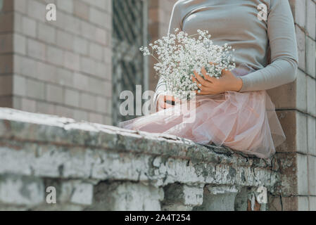 Frau in rosa spitze Rock mit weißen Blumen in den Händen Blumenstrauß sitzt auf der Treppe. Stockfoto