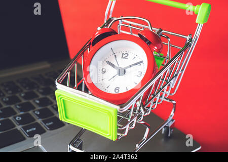 Warenkorb und Wecker auf Laptop auf rotem Hintergrund, Ansicht schließen Stockfoto