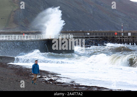 Aberystwyth, Ceredigion, Wales, UK. 16 Okt, 2019. UK Wetter: windigen Morgen mit Sonnenschein in Aberystwyth als Mann Spaziergänge am Strand, während die Wellen gegen das Meer die Abwehrkräfte. Credit: Ian Jones/Alamy leben Nachrichten Stockfoto