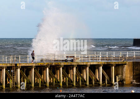 Aberystwyth, Ceredigion, Wales, UK. 16 Okt, 2019. UK Wetter: windigen Morgen mit Sonnenschein in Aberystwyth als Person Joggen entlang der Holzsteg, während die Wellen gegen das Meer die Abwehrkräfte. Credit: Ian Jones/Alamy leben Nachrichten Stockfoto