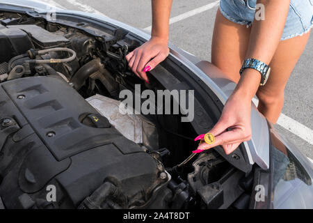 Die Frau in der Nähe des Auto Motorhaube. Junge Mädchen in überdachte Parkplätze, steht in der Nähe Auto mit angehobenen Motor haube, Kontrollen Motor Ölstand im Motor, inspiziert Stockfoto