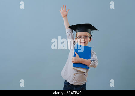 Redhead erster Sortierer Junge in Gläsern und Student hat hob seinen Arm über Blau Stockfoto