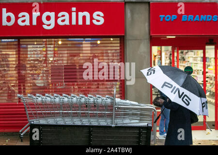 B&M-Geschäfte, B&M-Geschäfte, B&M-Geschäfte, B&M-Geschäfte, große Schnäppchen, große Ersparnisse, B&M-Schilder, B&M-Schnäppchen mit Gelenkwagen; Frau, die während schwerer Duschen einen Discounterladen mit Hauptgeschäften passiert. Sintflutartige Regenfälle in der Innenstadt, während Pendler und Käufer die Straßen der Stadt in windigen Bedingungen besuchen. Credit:MediaWorldImages/AlamyLiveNews Stockfoto