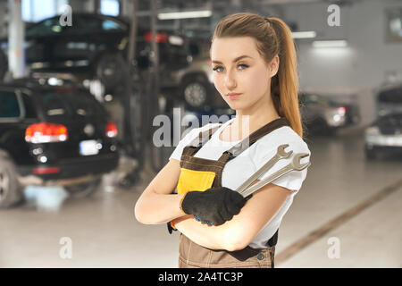 Charmant, schöne Mädchen, dass Schlüssel, auf Kamera posieren. Hübsche junge Frau arbeitet als Mechaniker im Autoservice, trug im weißen T-Shirt und Overalls. Stockfoto