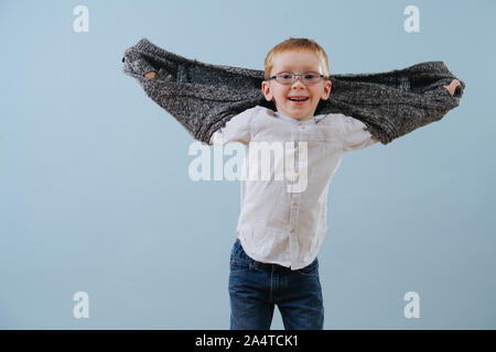 Porträt eines niedlichen kleinen ginger Junge in Gläser spielen mit Pullover über Blau Stockfoto