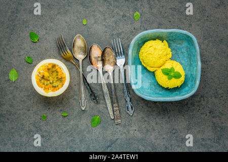 Die Zusammensetzung von Speiseeis Passionsfrucht Aroma in vintage Schüssel setup auf dunklem Stein Hintergrund. Passionsfrüchte mit Pfeffer Minze und Utensilien. Stockfoto