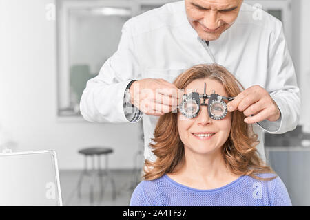 Attraktive Frau mit Brille mit Linse für die Überprüfung der Vision in der Klinik. Weiblichen erwachsenen lächelnd und suchen die Buchstaben für die Prüfung der Anblick in optischen Speichern. Konzept der Augenheilkunde. Stockfoto