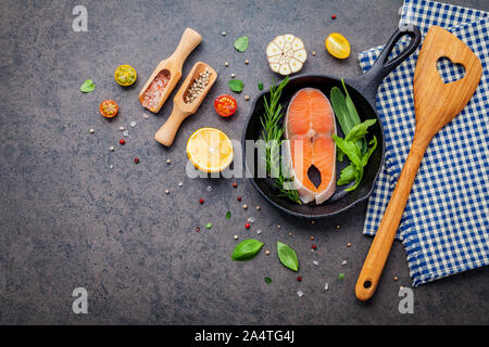 Lachsfilet in alten Gusseisen skille auf dunklem Stein Hintergrund. Zutaten für die Herstellung von steak Konzept mit kopieren. Verschiedene Kräuter und Gewürze rose Stockfoto