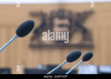 Stuttgart, Deutschland. 15 Okt, 2019. Die Mikrofone sind in Zimmer 2 des Oberlandesgericht (OLG Stuttgart) gelegen, mit dem Wappen von Baden-Württemberg an der Wand hängen. Credit: Sebastian Gollnow/dpa/Alamy leben Nachrichten Stockfoto