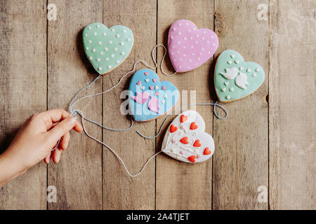 Eine weibliche Hand hält eine Zeichenkette von Herzen Cookies wie Luftballons Stockfoto