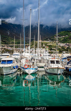 Yachten vor Anker in der Küstenstadt Arenzano, Italien, aus Wasser, das gegen die grünen Hügeln mit niedrigen Wolken gesehen Stockfoto