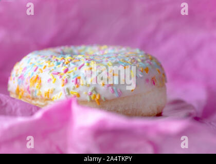 Makro Kopf auf Abbild eines einzigen Donut mit bunten Streuseln aus rosa Hintergrund für Kopie Raum Stockfoto