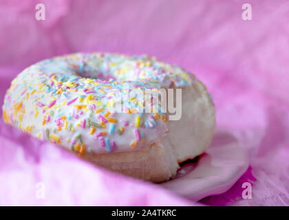 Makro Kopf auf Abbild eines einzigen Donut mit bunten Streuseln mit einem Bissen aus rosa Hintergrund für Kopie Raum genommen Stockfoto