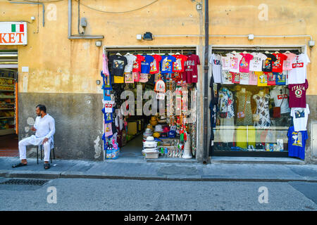 Blick auf die Straße mit einem ausländischen Ladenbesitzer vor seinem Souvenirshop im historischen Zentrum der berühmten Stadt Pisa, Toskana, Italien sitzen Stockfoto