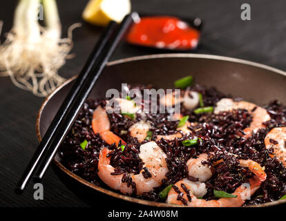 Schwarzer Reis mit Shrimps und grüne Zwiebel in einer Pfanne auf schwarzem Hintergrund gekocht. Ansicht von oben mit der Kopie Raum Stockfoto