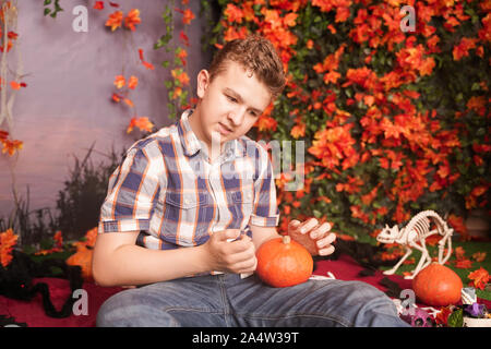 Foto von zornigen jungen Mann auf Halloween Tragen klassische Plaid Shirt Holding orange Kürbis auf Straße Hintergrund mit Blätter im Herbst. Stockfoto