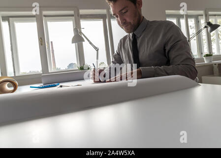 Architekt, Designer oder Zeichner bei der Arbeit im Büro auf einem großen Entwurf oder Plan in einer 7/8-Low Angle View über den Tisch mit kopieren. Stockfoto