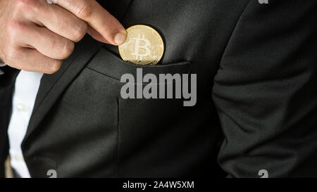 Geschäftsmann einen Bitcoin in seine Jackentasche, in der Nähe zu sehen, auf seine Finger und die Münze. Stockfoto