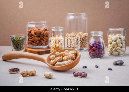 Verschiedene Bohnen und Nüsse in das Glas auf braunen Hintergrund. mung Bean, Erdnuß, rote Kidney-bohnen, Lotus Samen, Mandel, Hirse und Braun pinto Bohnen. Stockfoto