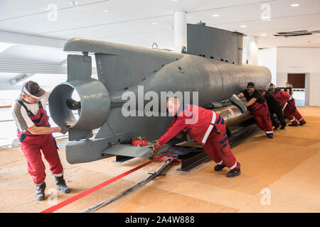 Bremerhaven, Deutschland. 16 Okt, 2019. Arbeitnehmer push ein Miniatur-U-Boot der "Deal" Art von Weltkrieg II aus seinem alten Platz im Deutschen Schiffahrtsmuseum in das Fenster vorne, so dass es von dort in das Erdgeschoss gehoben werden können. Nach einer umfangreichen Rekonstruktion, Museum die Ausstellung wird ein Platz im Erdgeschoss finden. Um die 12 Meter lange und 12 Tonnen schwere U-Boot Es zu transportieren, eine grosse Fensterfront wurde entfernt. Quelle: Jörg Sarbach/dpa/Alamy leben Nachrichten Stockfoto