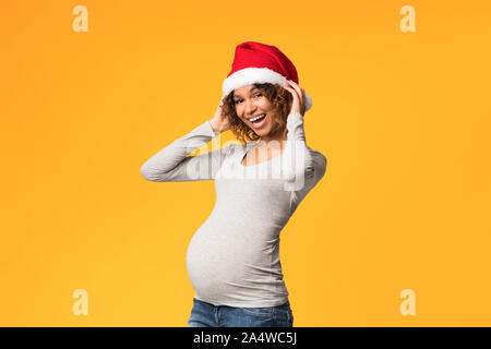 Junge schwangere Frau in Santa Hut, gelben Hintergrund Stockfoto