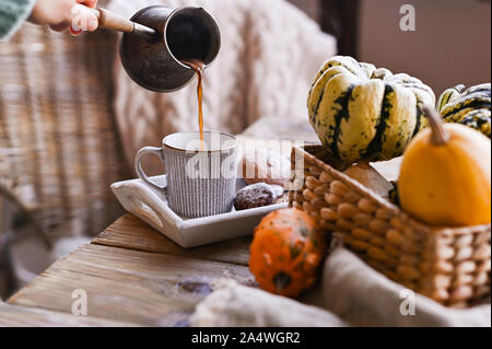 Herbst und Winter hausgemachte noch leben. Ein Mädchen in einem gestrickten Pullover gießt frisch gebrühten Kaffee in eine Tasse. Das Konzept der Atmosphäre und Dekor. Holztisch keks Kekse mit Zimt Stockfoto