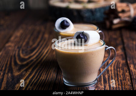 Happy Monster, Pumpkin spice Latte mit Schlagsahne und großen Marshmallow Auge auf der Oberseite, Halloween Dessert, eibisch Smiley auf rustikalen Holzmöbeln tab Stockfoto