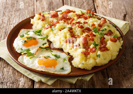 Hausgemachtes Kartoffelpüree mit Speck und Petersilie serviert mit Spiegeleier auf einem Teller auf den Tisch closeup. Horizontale Stockfoto