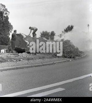 1967, historisch, zwei männliche Baumchirurgen mit Kettensägen neben und auf einem großen Baum, der von einer Straße gefallen ist, in England, Großbritannien. Stockfoto