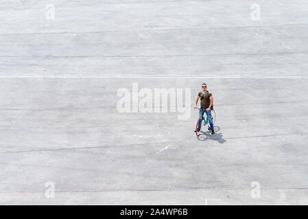 Junger Mann, der mit seinem Fahrrad auf ein Quadrat (Copyspace) Stockfoto