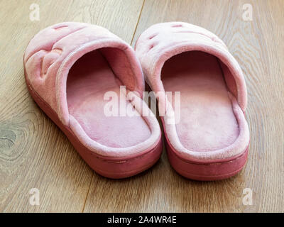 Paar weiblicher Haus Hausschuhe auf einem braunen Holzboden. Gemütlich, warm und gemütlich, Rosa- Schuhe. Ansicht von hinten. Stockfoto