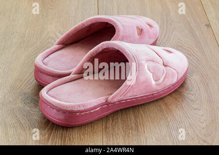 Paar rosa weiblichen Haus Hausschuhe auf einem braunen Holzboden. Gemütliche, warme und bequeme Schuhe im Inland. Von der Seite. Stockfoto