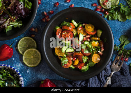 Frischer Salat mit Tomaten, Gurken und Kräuter, flach über dem Salat ist in einem schwarzen Schüssel, und es gibt andere Schüsseln mit Zutaten um ihn herum. T Stockfoto