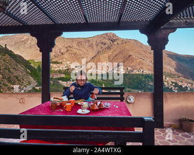 Kaukasische blonde Mädchen hlaving typisch marokkanische Frühstück mit amlu und hausgemachte Pfannkuchen auf der Terrasse mit schöner Aussicht in Imlil Hohen Atlas Moroc Stockfoto