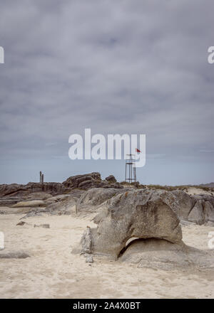 In der Nähe von Felsen am Strand ein Tag mit stürmischen Wolken im Hintergrund. Bei einem Abstand der Turm der Rettungsschwimmer Felsen, Sand und Wasser. Stockfoto