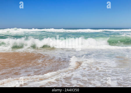 Low Angle Frontalansicht des kleinen schäumenden Ozean Wellen an einem Sandstrand an einem sonnigen Tag. Stockfoto