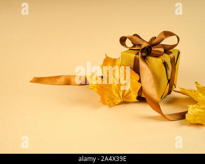 Ein einsamer Golden Leaf und lackiert Blatt in das gelbe Metall, die Platz für Text neben einem Geschenk Box und goldenen Band. Stockfoto