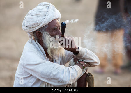 Rajasthani Mann Rauchen ein Chillum (Rohr) von Haschisch in Pushkar Camel Fair, Rajasthan, Indien Stockfoto
