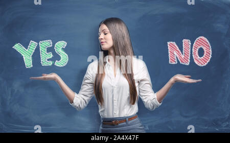 Schöne Geschäftsfrau stehend mit offenen Handflächen zwischen großen bunten Worten 'Ja' und 'Nein' auf dunkelblauem Hintergrund geschrieben. Stockfoto