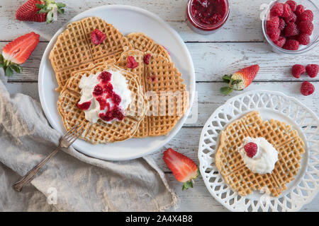 Waffeln mit frischen Himbeeren und Erdbeeren und Schlagsahne von oben, flach legen Vorausschau - gesehen. Es ist eine Glasschale mit ganzen Himbeeren Stockfoto