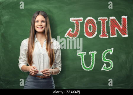 Junge schöne Frau, die in der Nähe der grossen hellen Worte "Join Us" auf grüner Tafel geschrieben Stockfoto