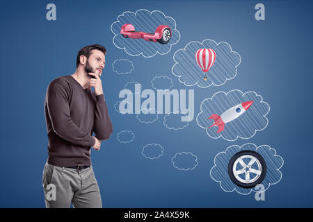 Ein Mann steht in der Nähe von gedankenblasen mit einer Rakete gefüllt, ein Autoreifen, ein heißes Gas Ballon und eine hyroscooter. Stockfoto