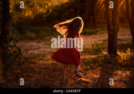 Mädchen läuft durch Bäume mit Licht hinter ihr Stockfoto