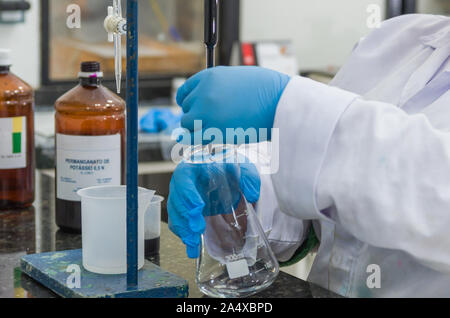 Frau Hände in schutzhandschuhen Reagenzglas in Händen halten produziert Chemie Test. Stockfoto